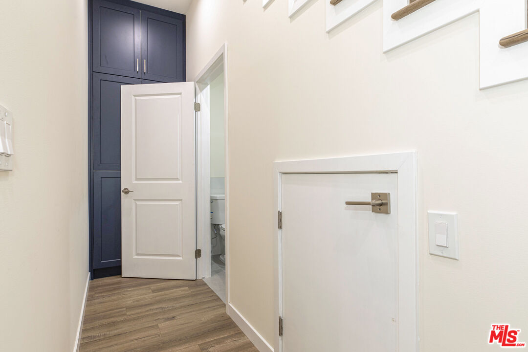 Hallway with dark blue built-in cabinets, wood-look flooring, and an open bathroom door.