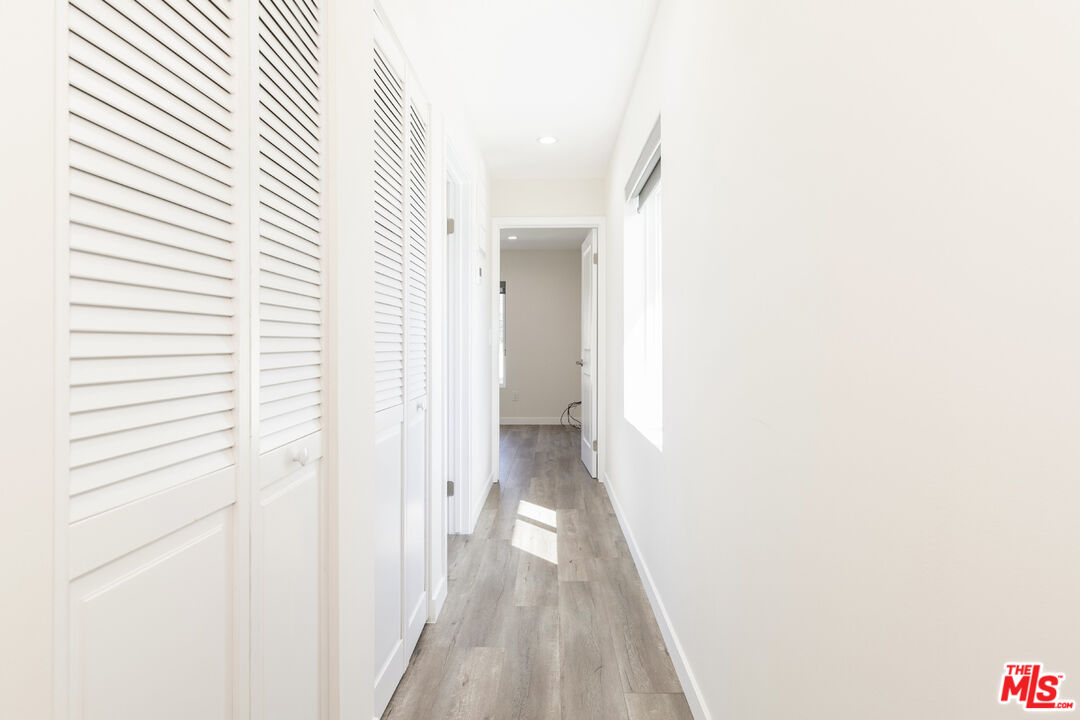 Bright hallway with white louvered closets, gray wood-look flooring, and sunlight through a side window.