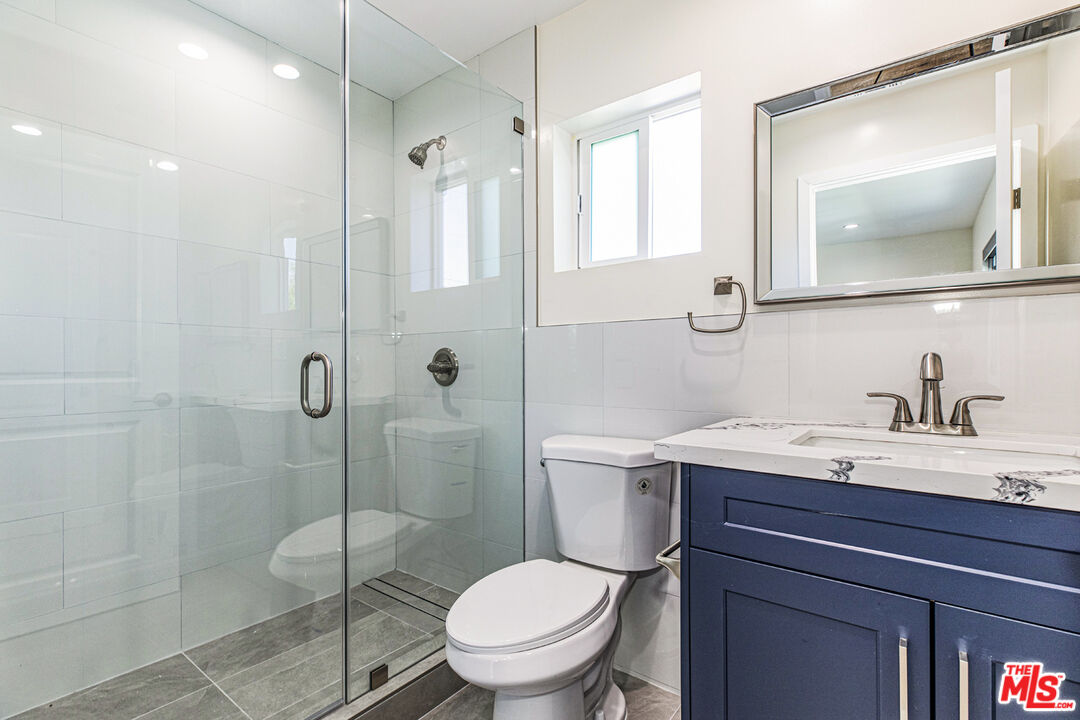Bathroom with a glass-enclosed shower and navy-blue vanity with a marble countertop.