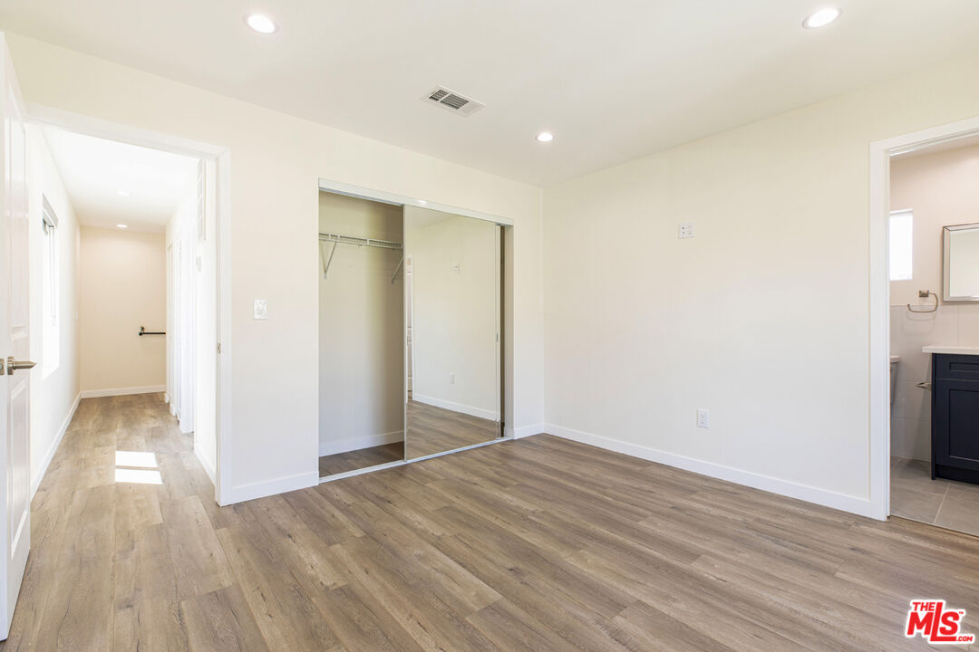 Vacant bedroom with wood-look flooring, mirrored closet doors, and an adjoining bathroom doorway.