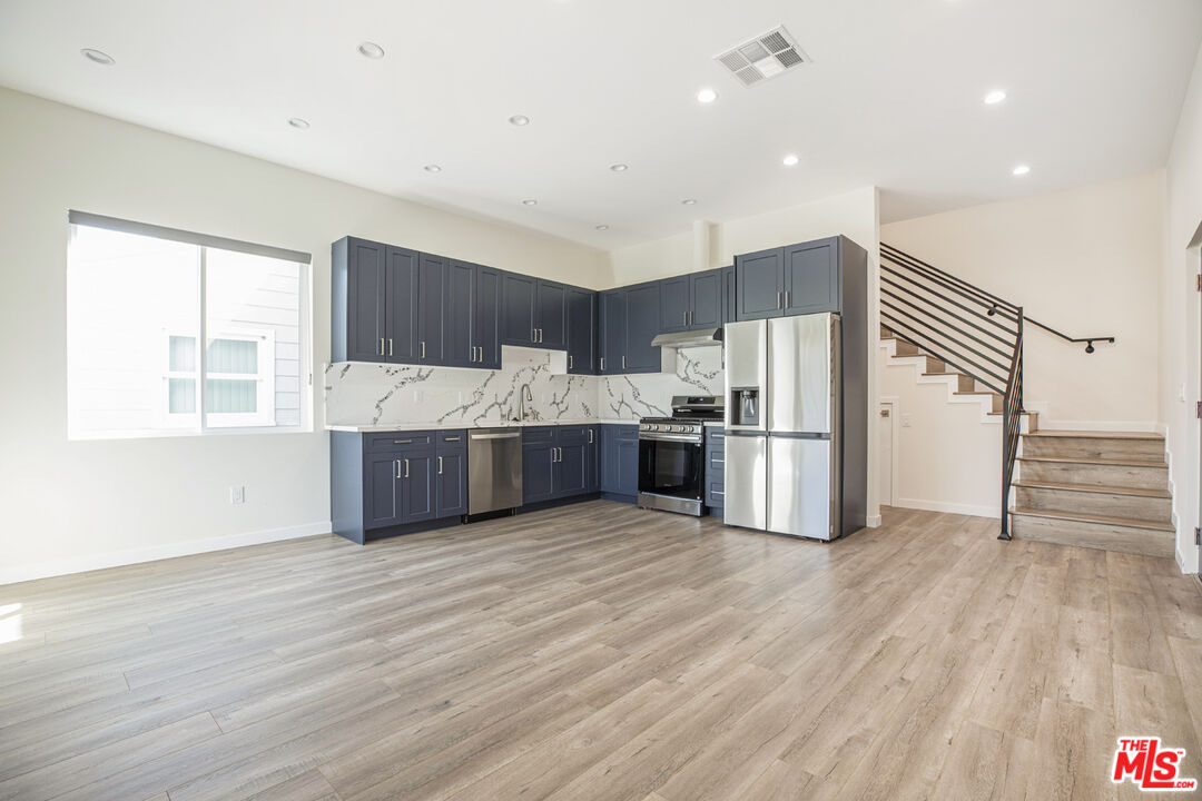 Open kitchen with dark blue cabinets, stainless steel appliances, and a staircase with black railing.