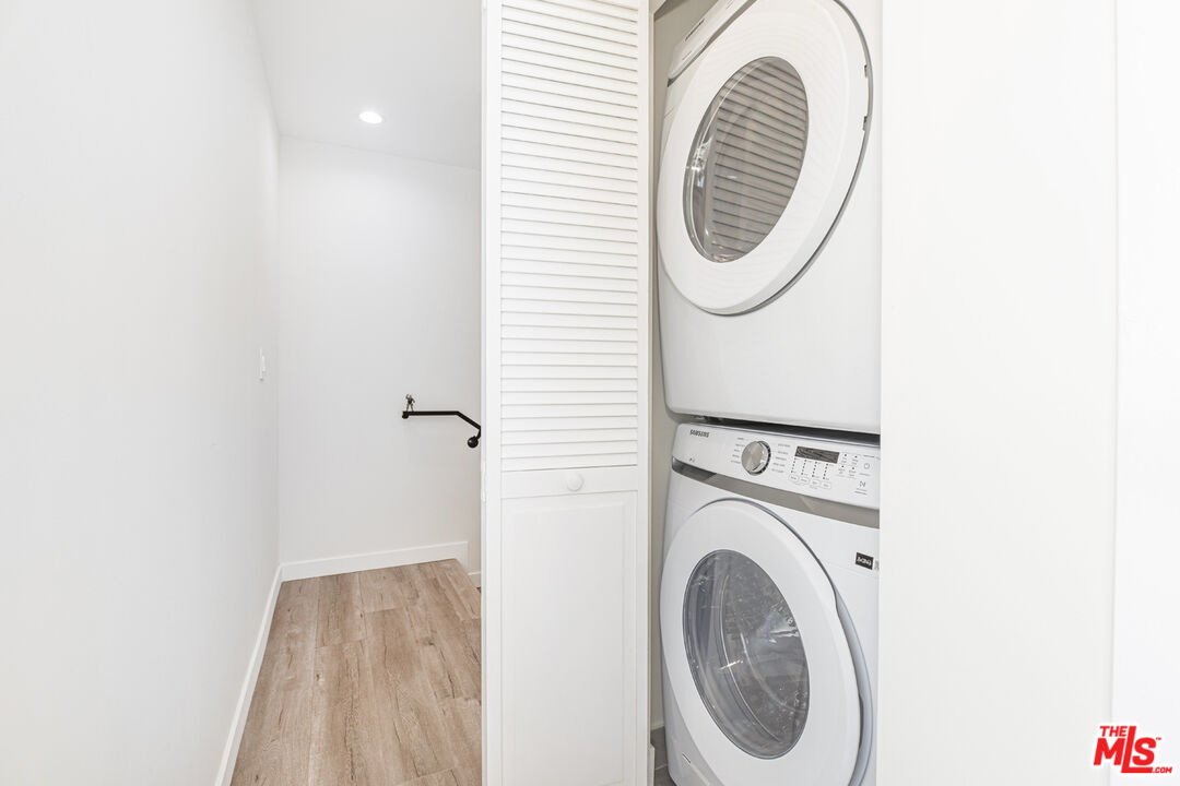 Laundry closet with stacked front-loading washer and dryer beside a narrow wood-look-floored passage.