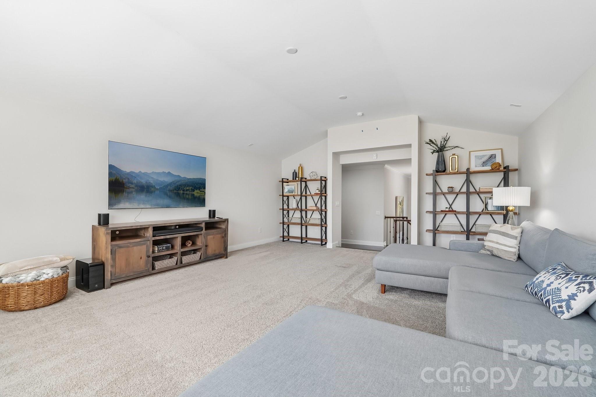 Furnished living room with a gray sectional, wall-mounted television, and open shelving.