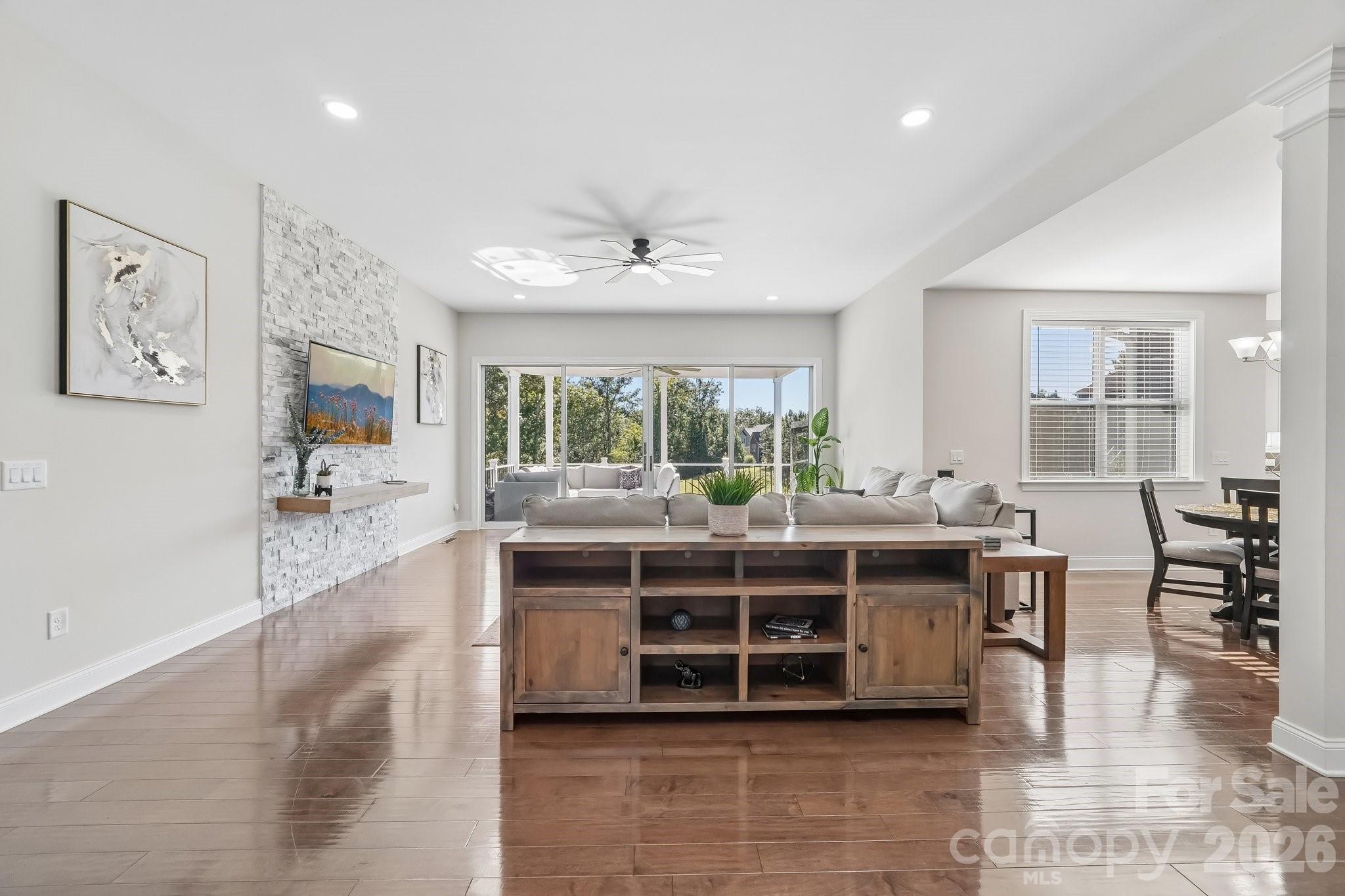 Furnished living room with glossy wood floors, white stone accent wall, and wide sliding glass doors.