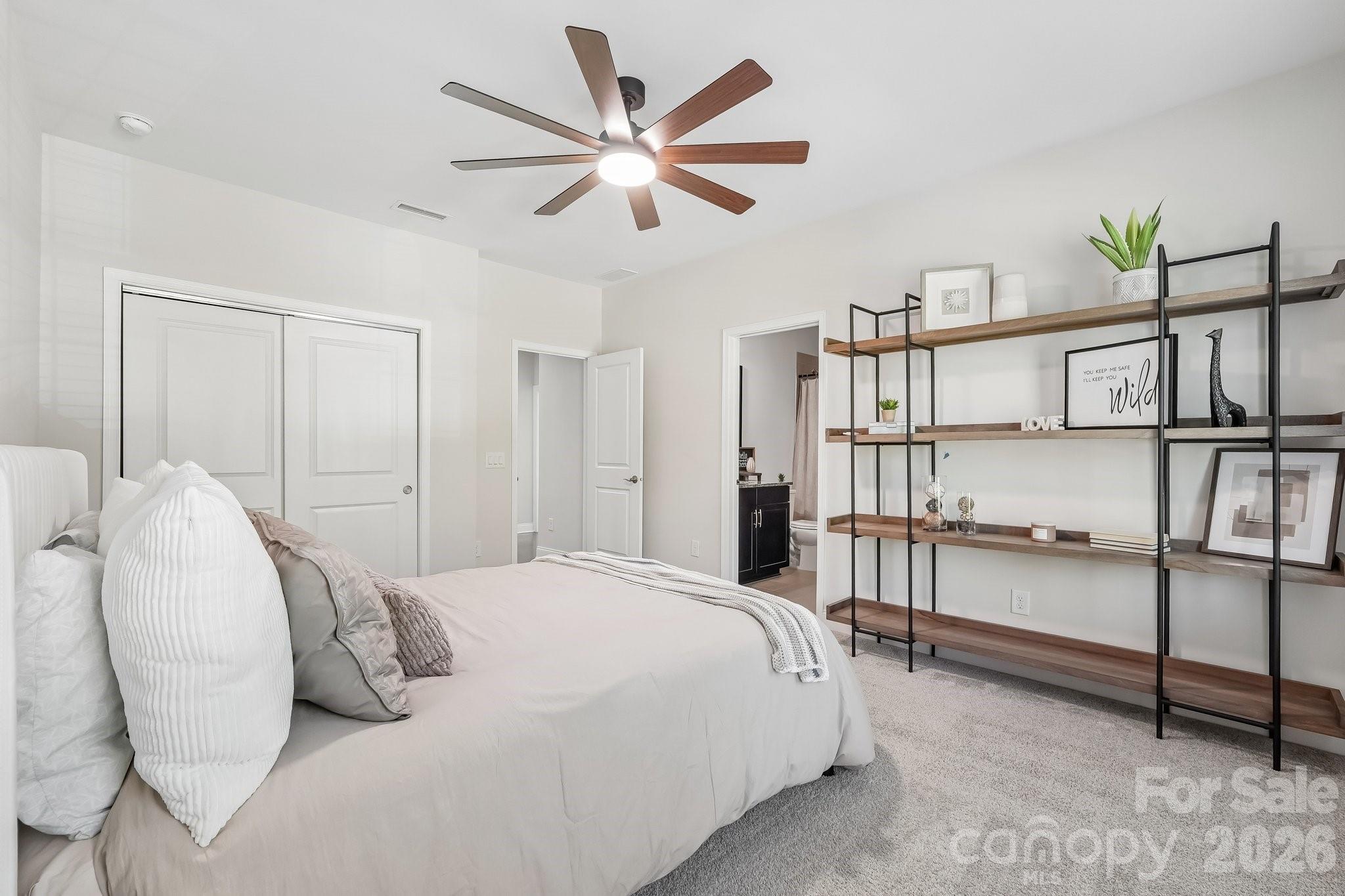 Staged bedroom with a white bed, wood-blade ceiling fan, and open shelving.