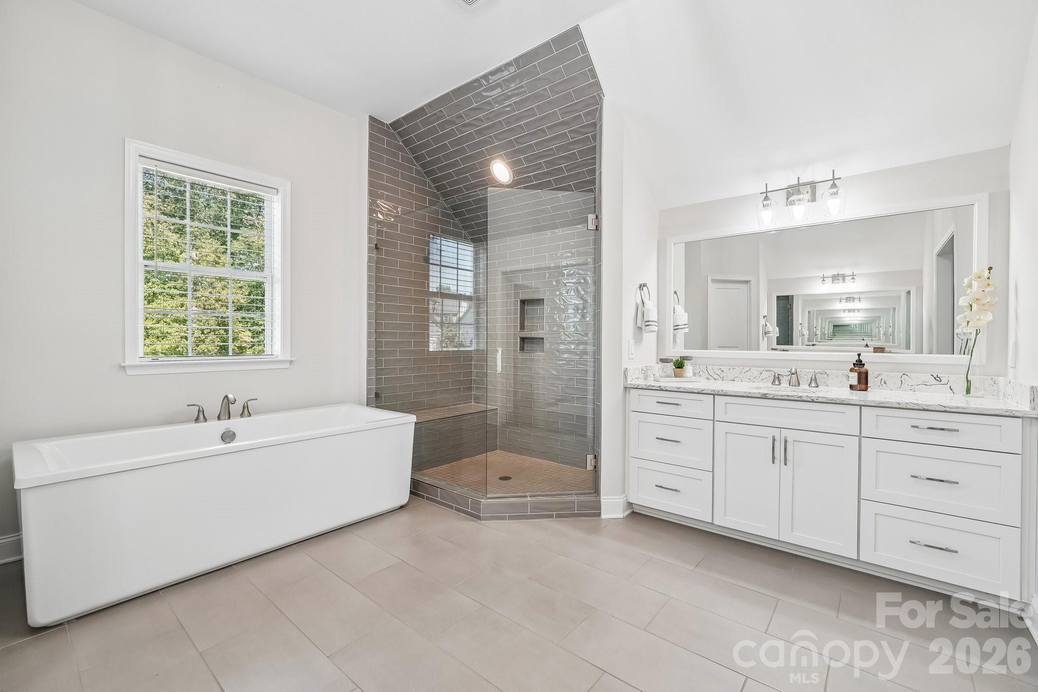 Modern bathroom with a freestanding tub, gray-tiled glass shower, and white double vanity.