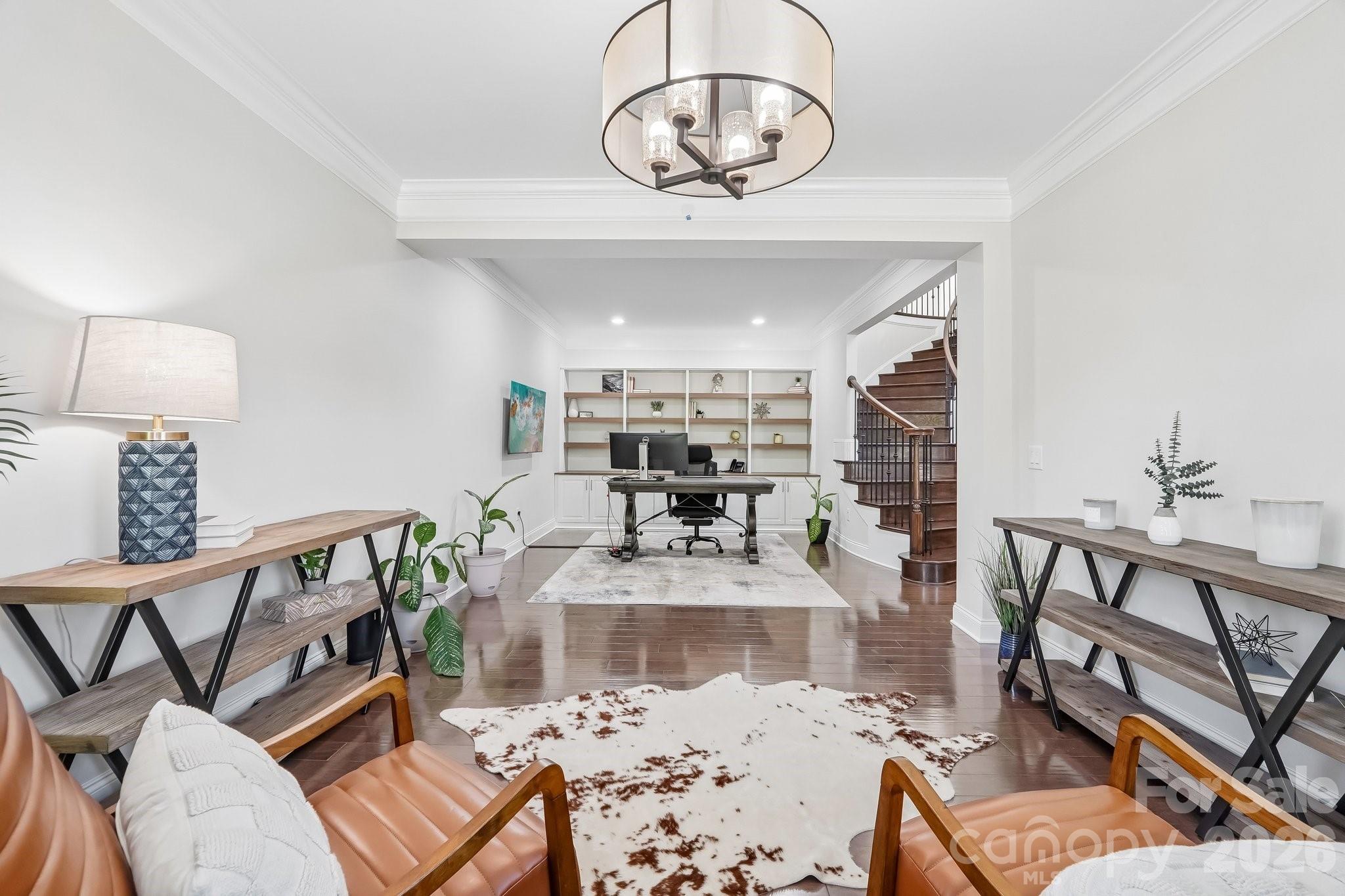 Staged home office with built-in shelves, leather chairs, and a curved staircase.