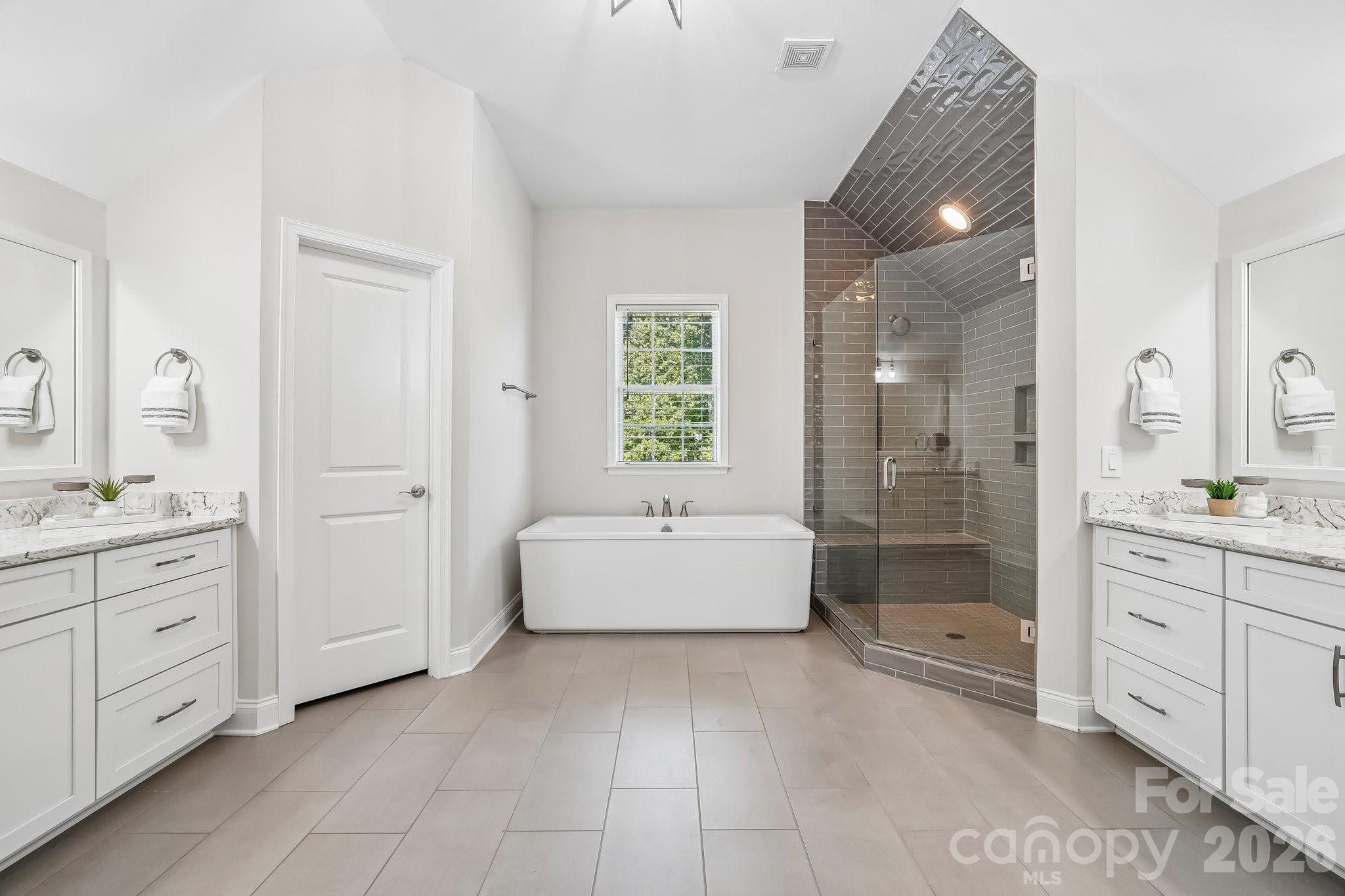Primary bathroom with a freestanding tub, glass-enclosed tiled shower, and double vanities.