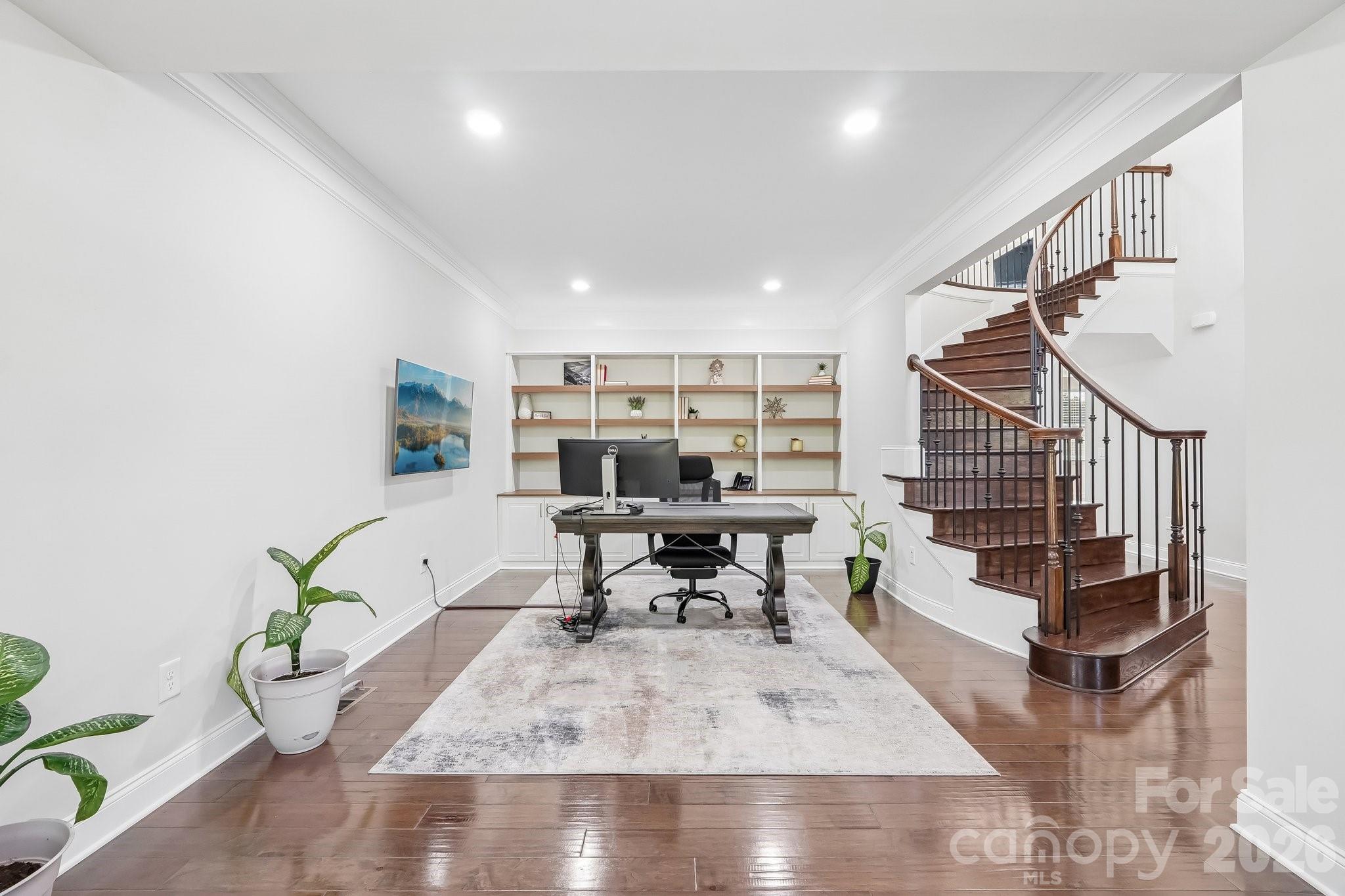 Home office with built-in shelves beside a curved dark wood staircase.