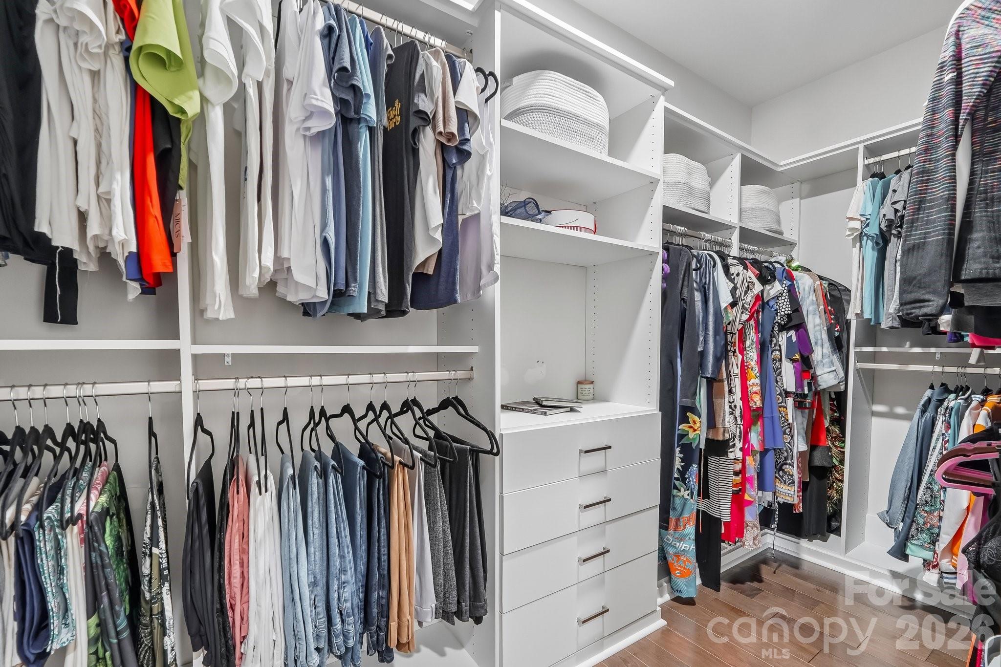 Walk-in closet with white built-ins, drawers, storage baskets, and clothes on multiple hanging rails.