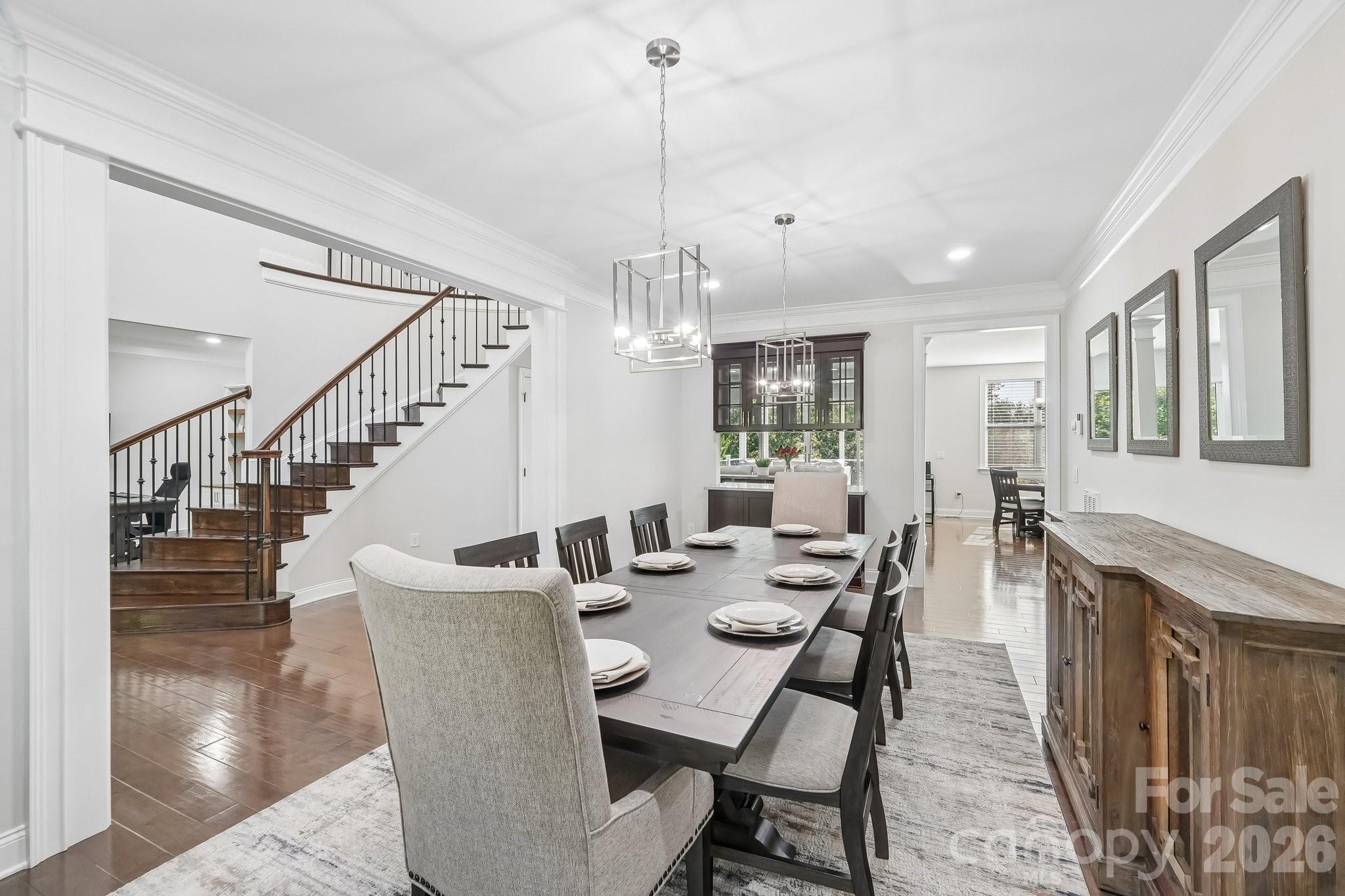 Dining room with a set table, dark wood staircase, modern pendant lights, and a long wooden sideboard.