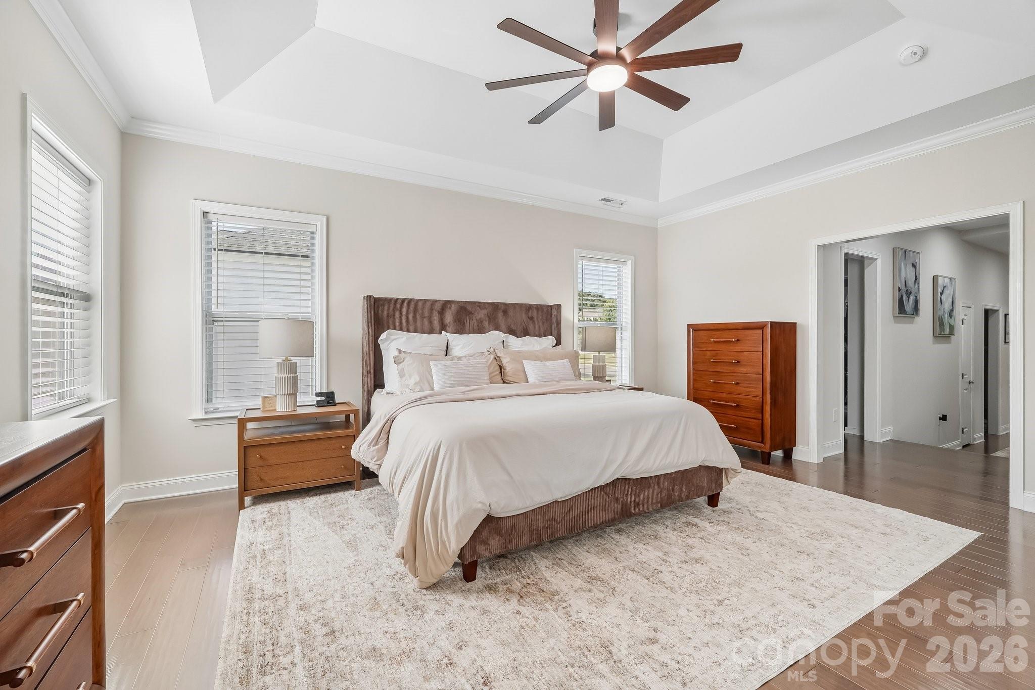 Furnished bedroom with a large bed, wooden dressers, and a high ceiling with a ceiling fan.