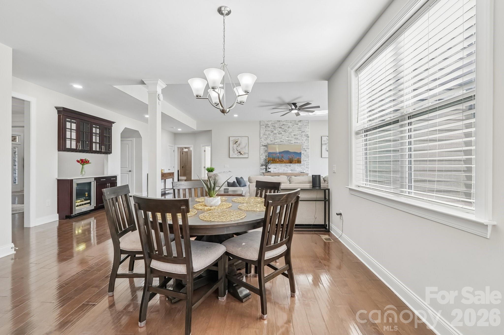 Dining room with a dark wood table beside a large window, opening to a living room with a stone fireplace.