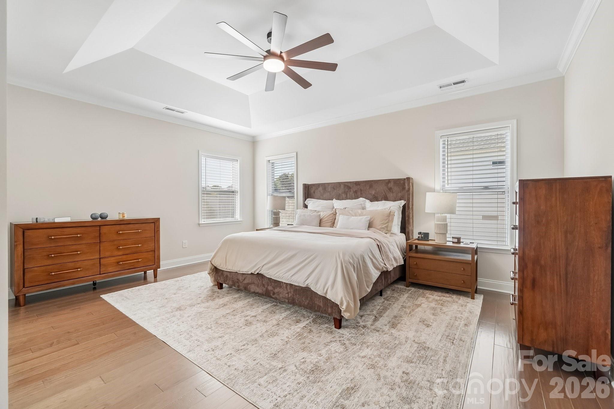Furnished bedroom with a large bed, matching wooden dressers, and a tray ceiling with a ceiling fan.