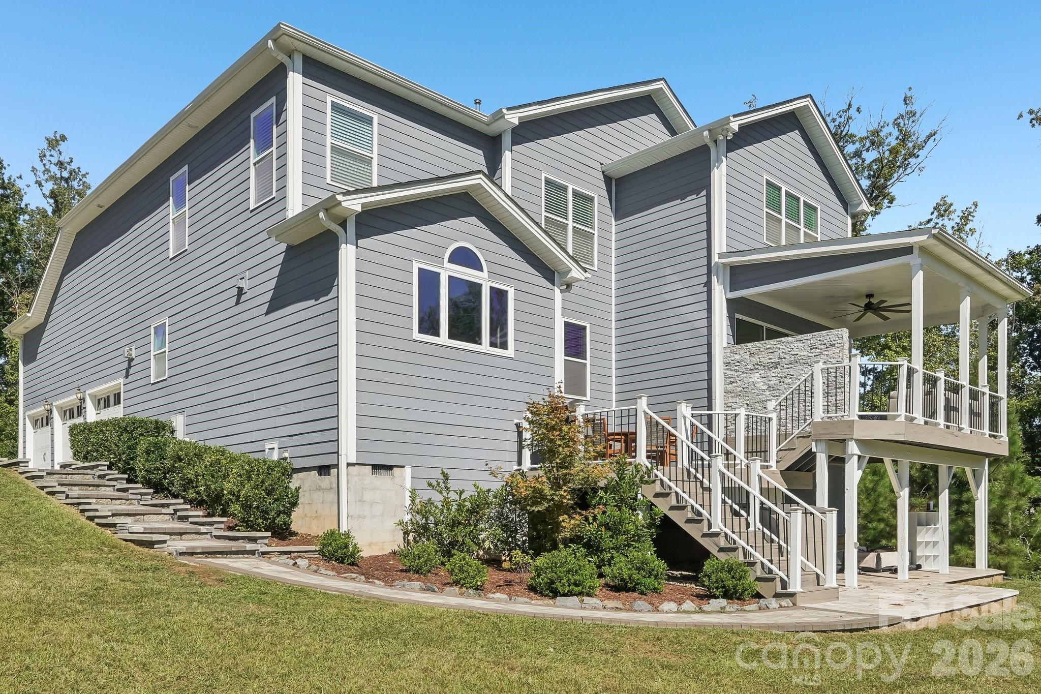 Gray two-story home with a raised covered deck, white railings, and landscaped lawn.