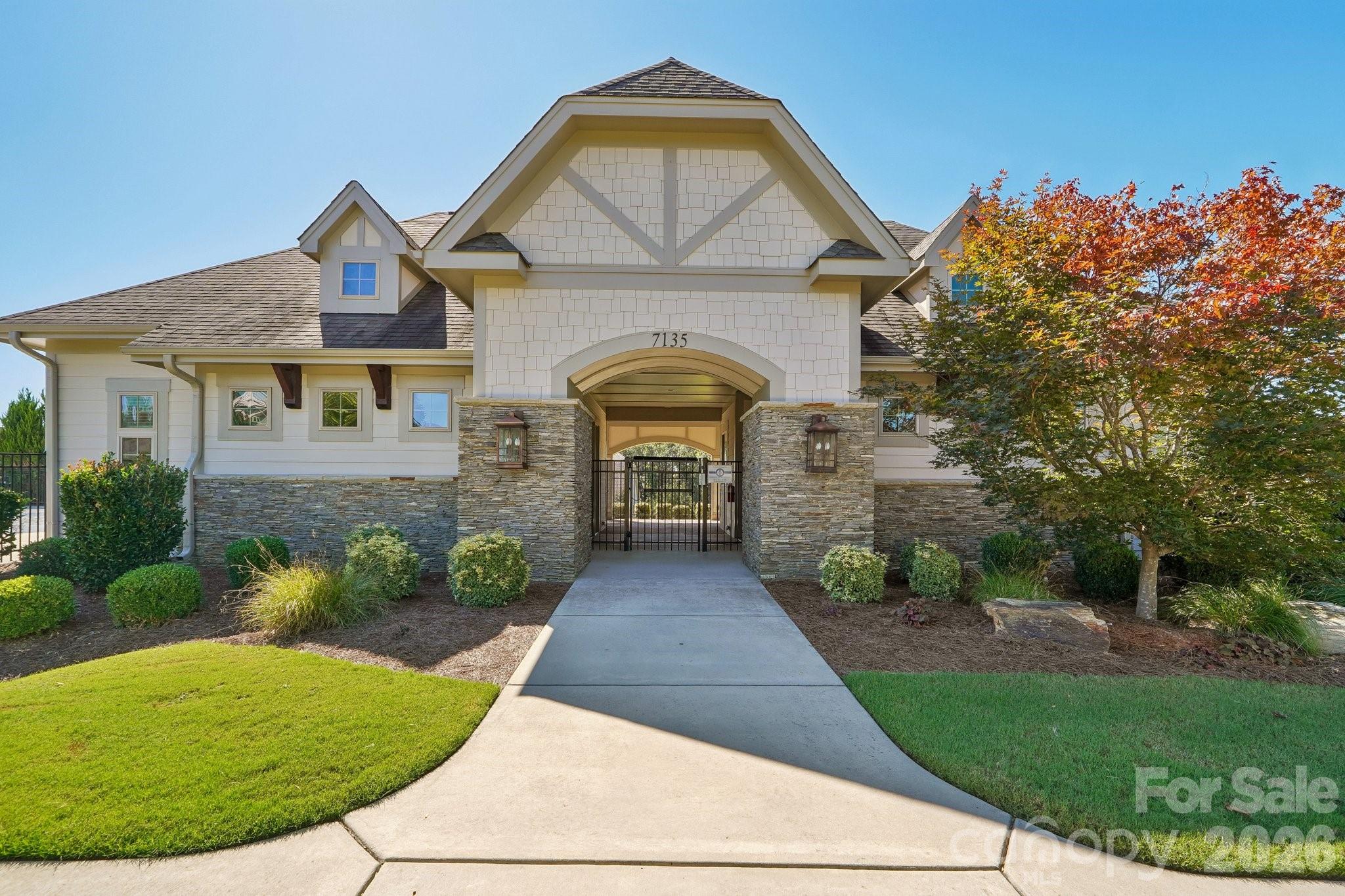 Light-colored home with stone veneer, an arched entrance, gated walkway, and autumn-colored tree.