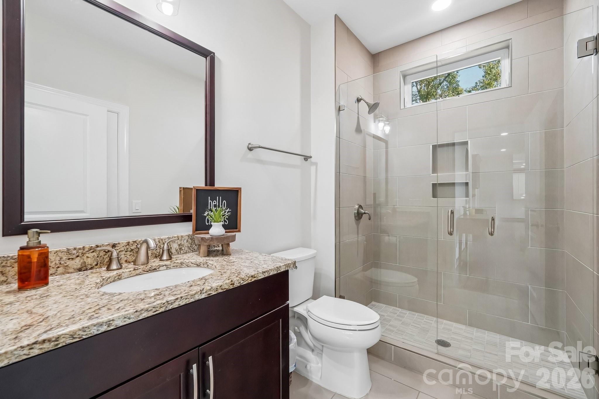 Bathroom with a granite-topped dark wood vanity and glass-enclosed tiled shower.
