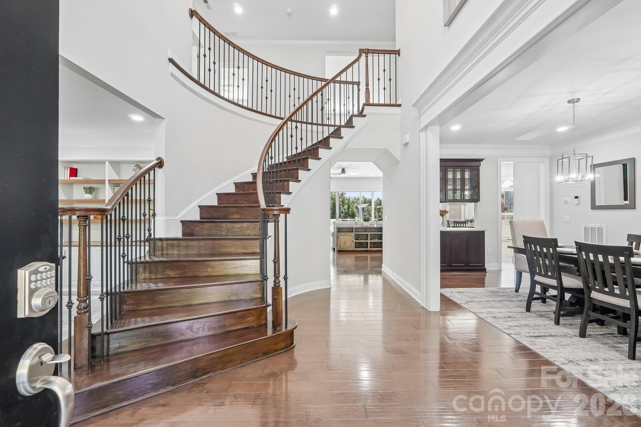 Entry hall with a curved wood staircase and iron balusters beside an adjoining dining room.