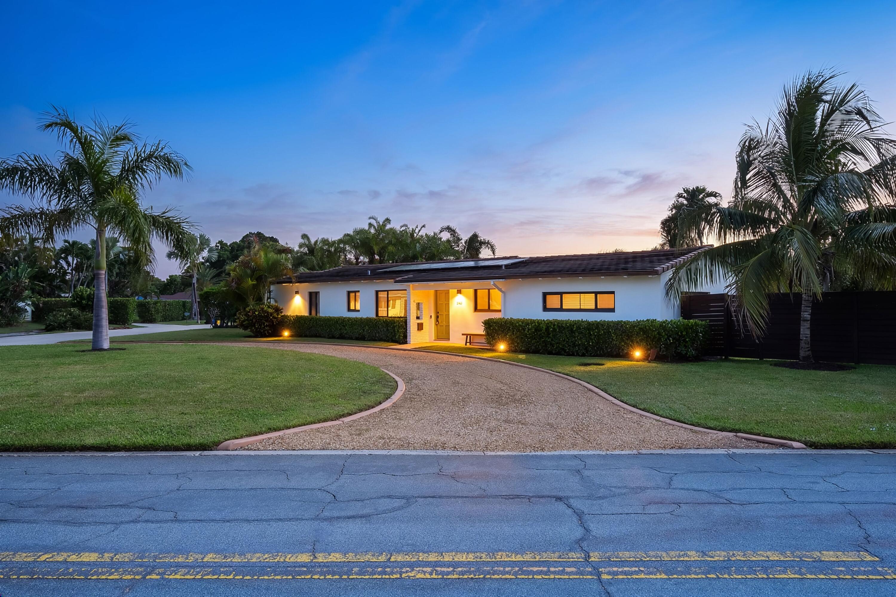 Single-story home with a curved driveway, trimmed lawn, and palm trees at dusk.