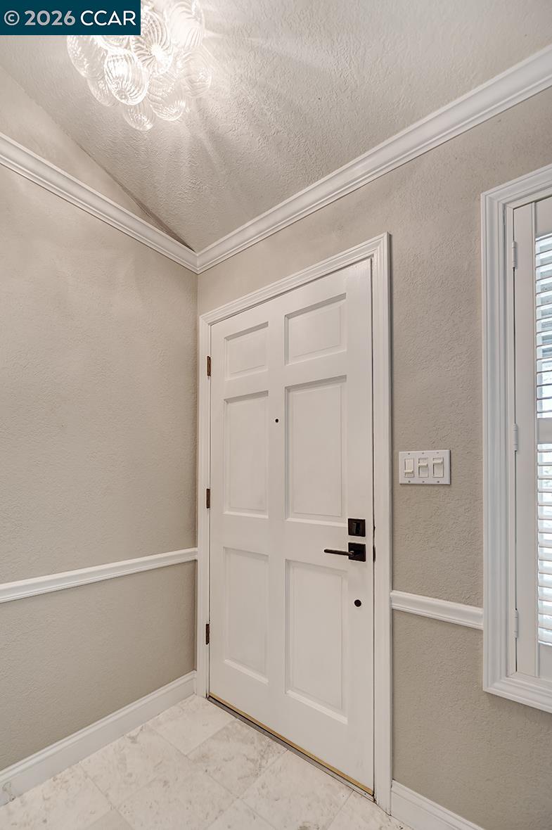Entryway with a white paneled front door, marble-look tile floor, and glass chandelier.