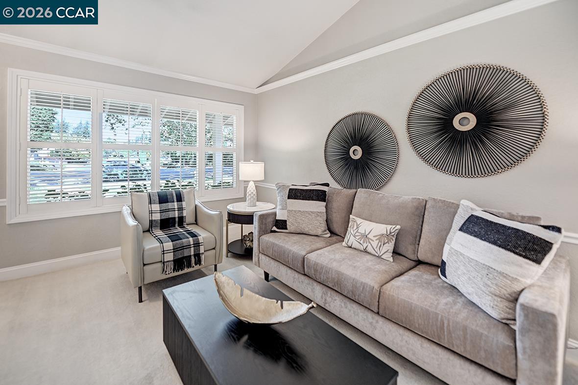 Furnished living room with a gray sofa, plaid armchair, and wide shuttered windows.