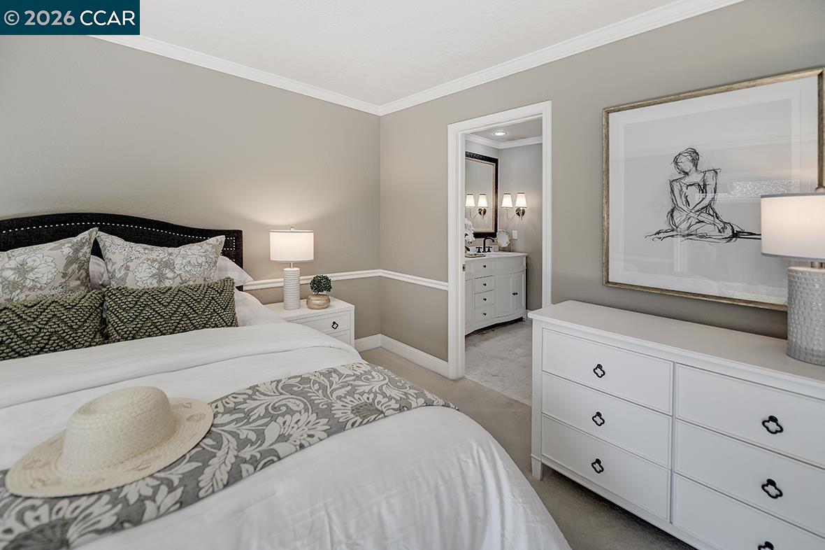 Staged bedroom with a white bed and patterned bedding, opening to an adjoining bathroom.