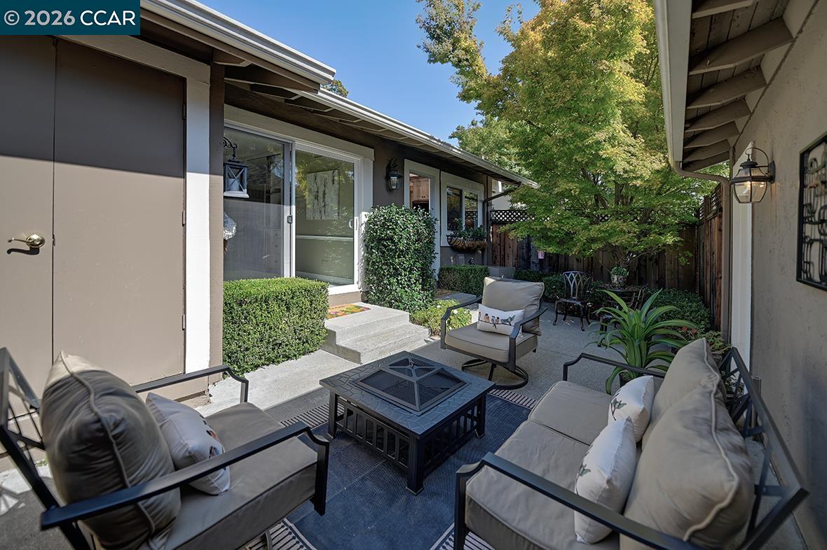 Furnished outdoor patio with cushioned seating, a coffee table, and leafy landscaping beside the home.