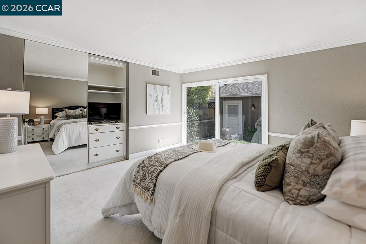Staged bedroom with mirrored closet doors and sliding glass doors opening to a patio.