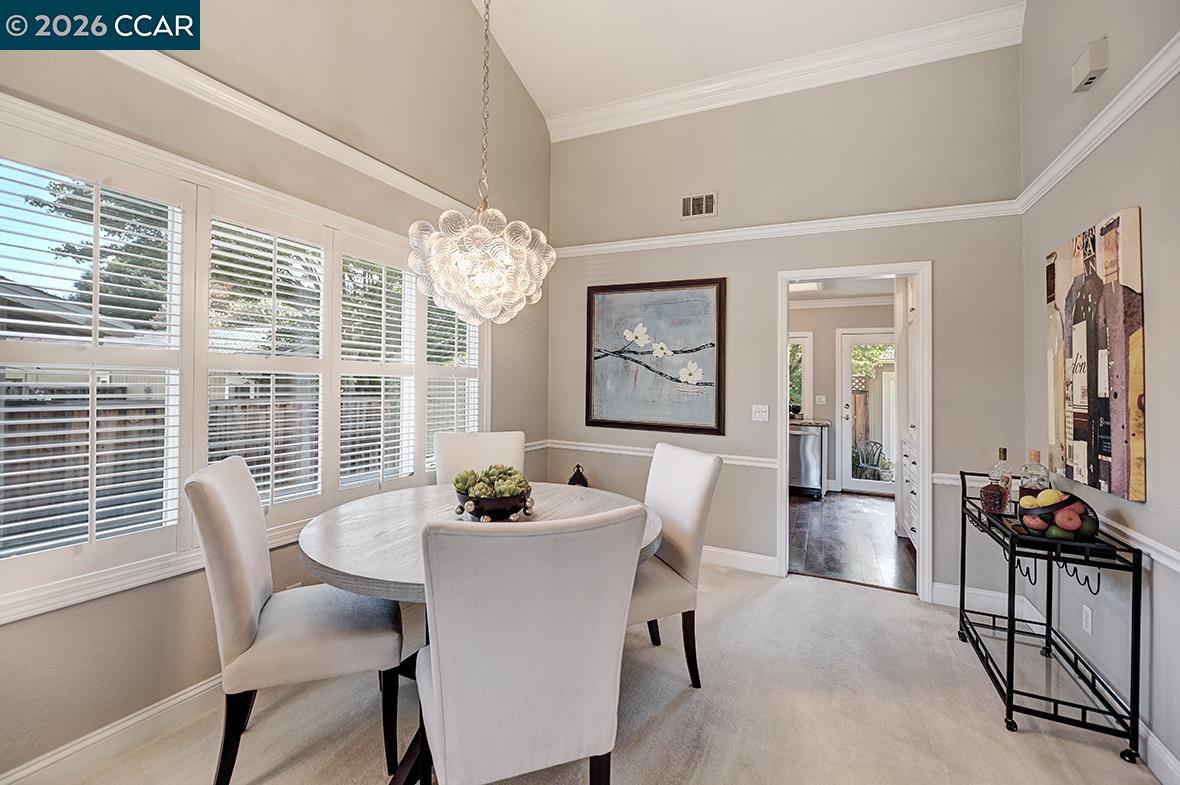 Dining room with a round table, sculptural chandelier, and tall windows with plantation shutters.