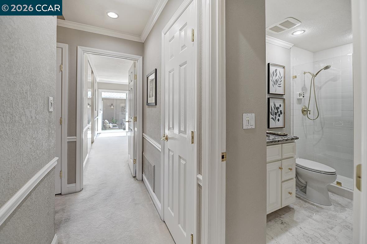 Hallway leading to a bathroom with a white tiled shower, vanity, and toilet.