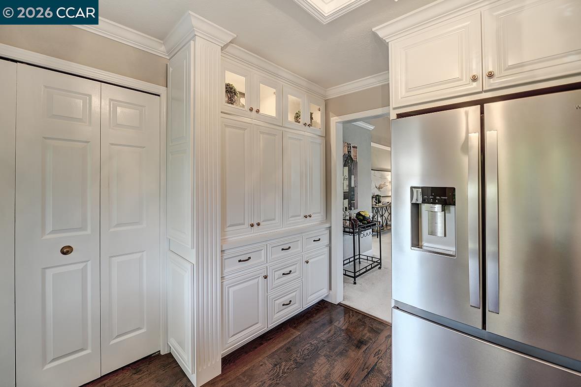 Kitchen with white paneled cabinetry, stainless steel refrigerator, and dark hardwood floors.