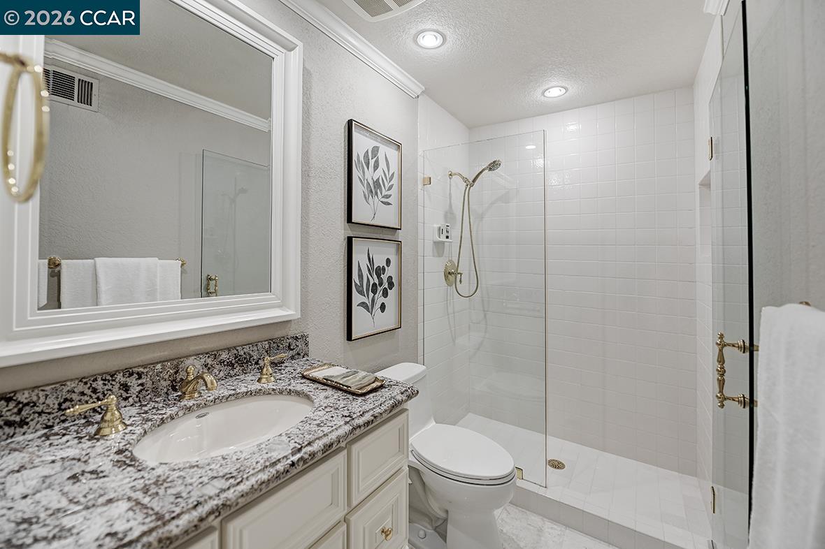 Bathroom with a granite vanity, framed mirror, and white tiled walk-in shower.