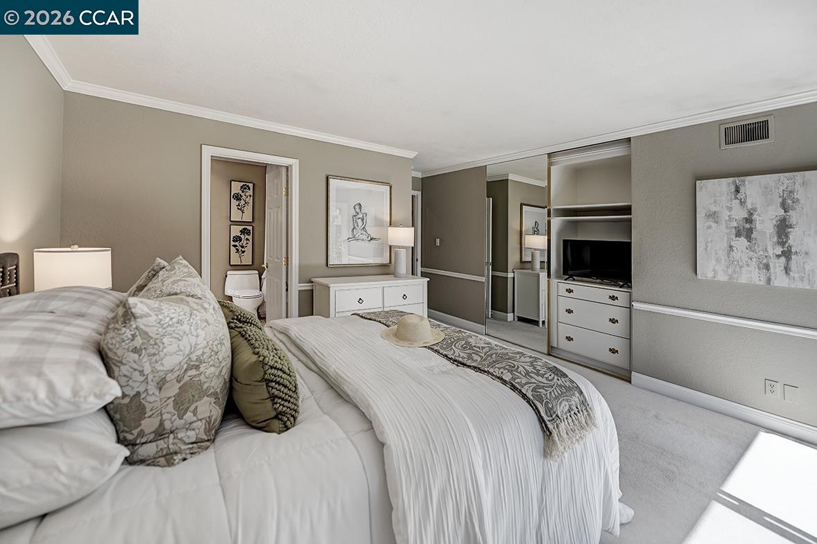 Staged bedroom with a white bed, mirrored closet doors, and a built-in TV cabinet.