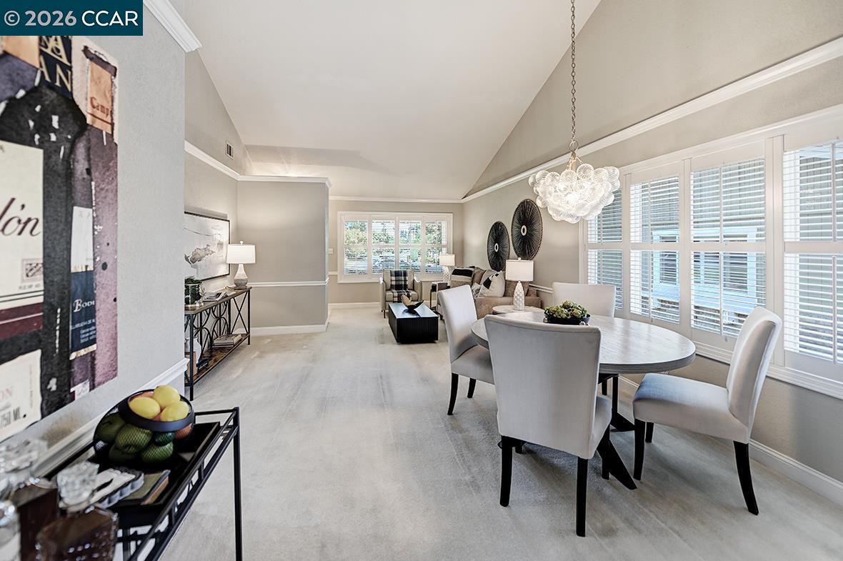 Open-plan living and dining room with a vaulted ceiling, chandelier, and wide windows with plantation shutters.