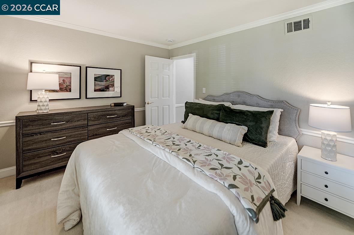 Furnished bedroom with a large bed, gray upholstered headboard, dark wood dresser, and matching bedside lamps.