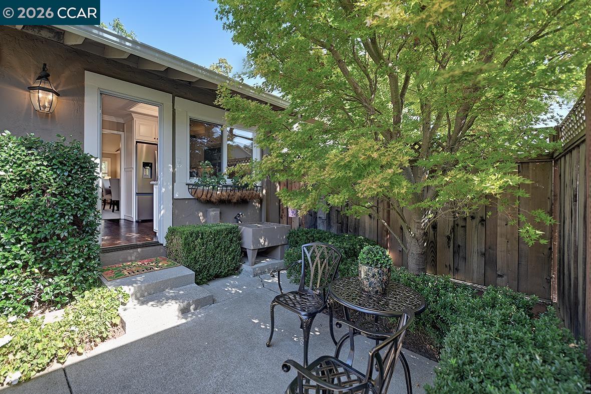 Outdoor patio with metal seating beneath a leafy tree beside the home.