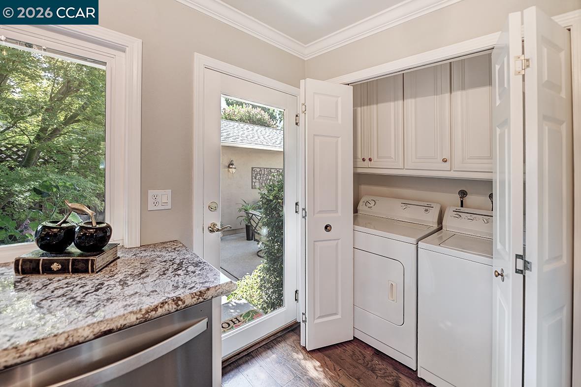 Laundry room with white washer and dryer, built-in cabinets, granite counter, and glass door.
