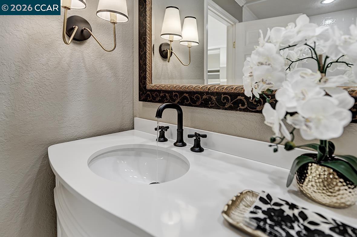 Bathroom vanity with a white oval sink, black faucet, ornate mirror, and white orchids.