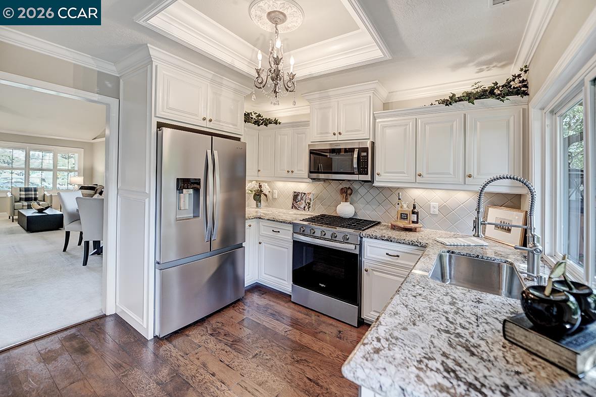 White kitchen with stainless steel appliances, granite counters, and a view into the adjoining sitting area.