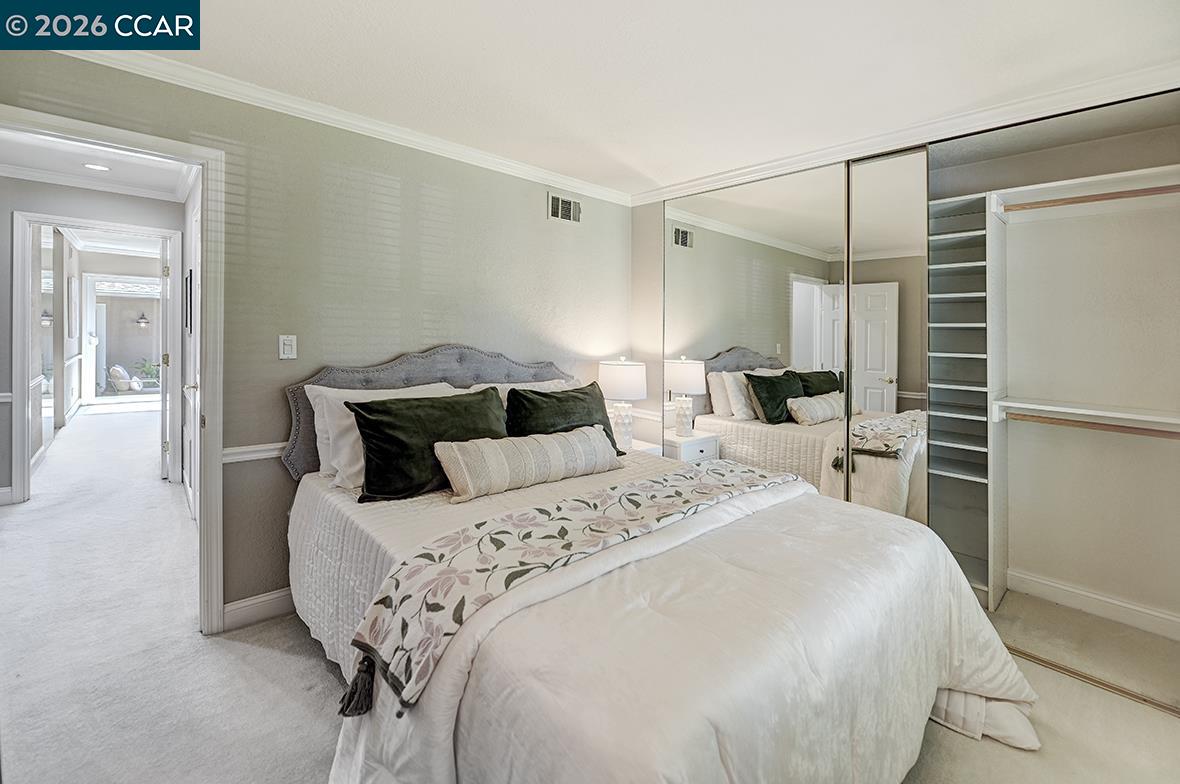 Furnished bedroom with mirrored closet doors and a large bed with dark green pillows.