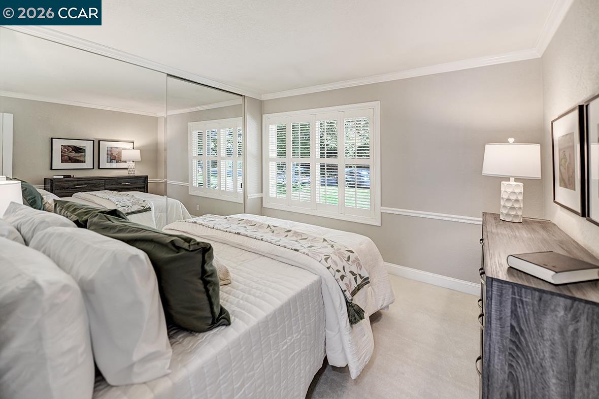 Furnished bedroom with two white beds, green accent pillows, and shuttered windows.