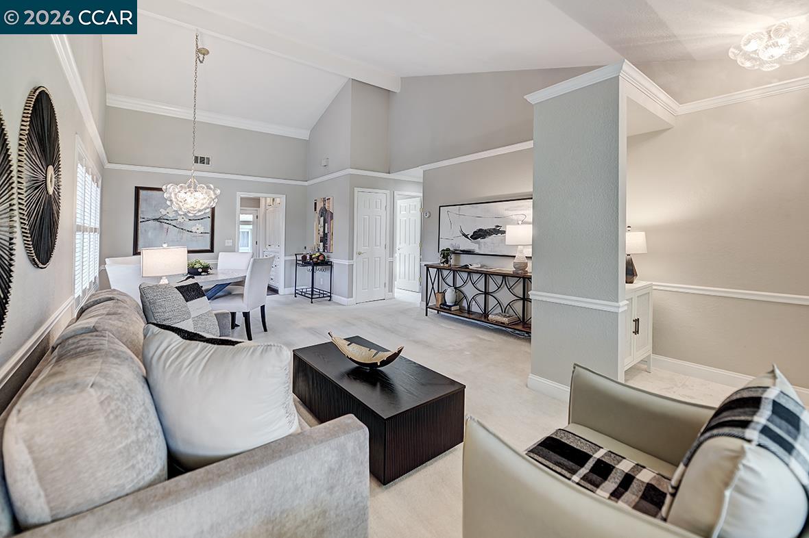 Living room with vaulted ceiling, pale seating, dark coffee table, and adjoining dining area.