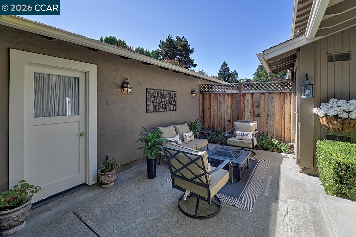 Furnished outdoor patio with cushioned seating, a striped rug, potted plants, and a wooden privacy fence.