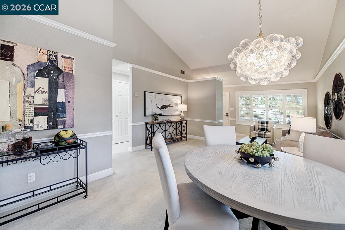 Dining room with a round table and sculptural glass chandelier beside a bright living area.
