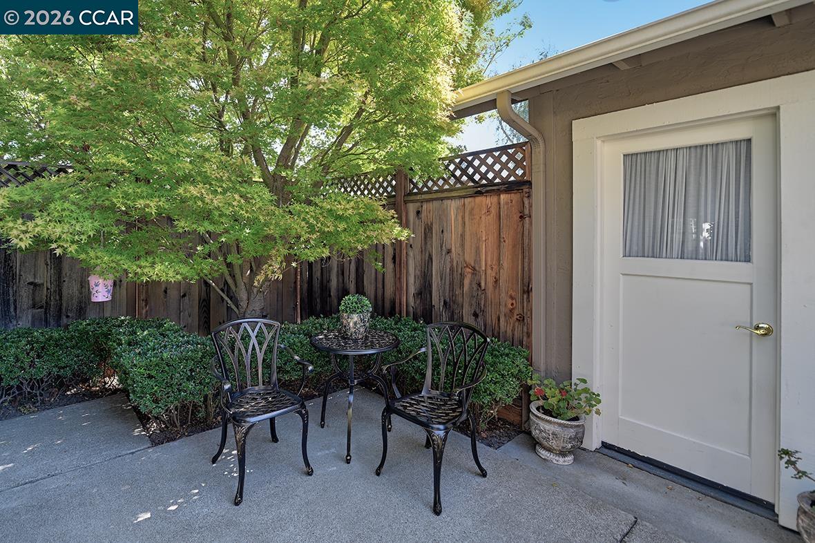 Patio with black metal table and chairs beneath a leafy tree beside a white exterior door.
