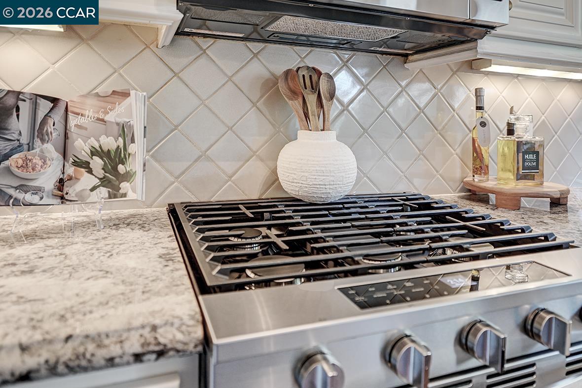 Kitchen gas range with stainless-steel finish, marble-patterned counters, and a pale diamond-tile backsplash.