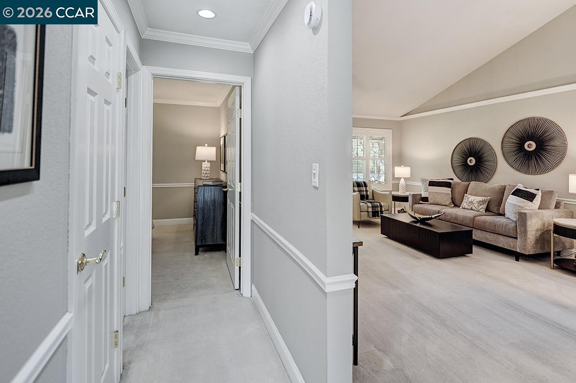 Living room with a beige sectional, dark coffee table, and circular wall art, viewed from the hallway.