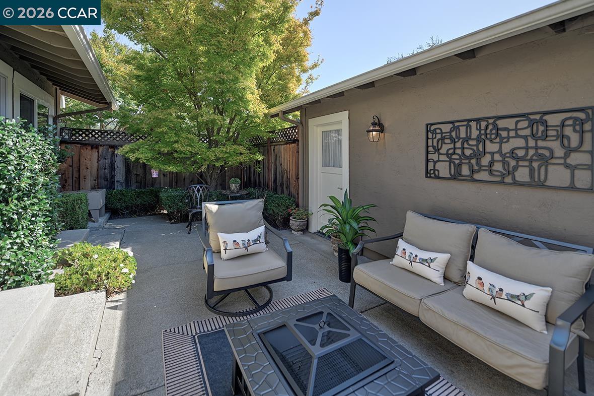 Furnished patio with cushioned seating, coffee table, leafy tree, and garden beds.