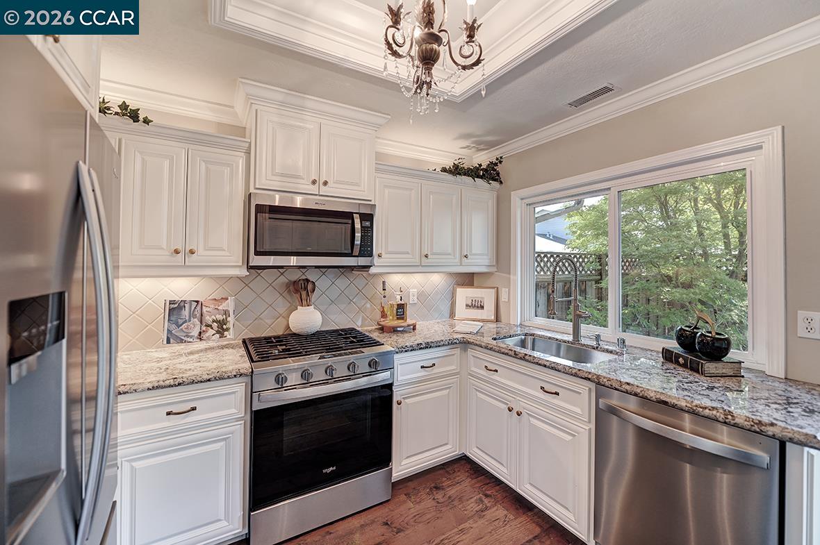 Kitchen with white cabinetry, granite counters, stainless appliances, and a window overlooking trees.