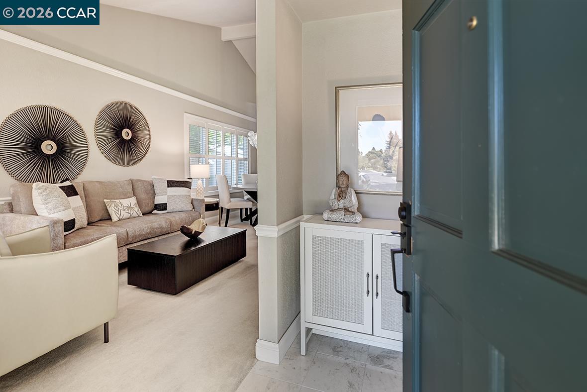 Furnished living room seen through an open teal front door, with a beige sofa and decorative wall discs.